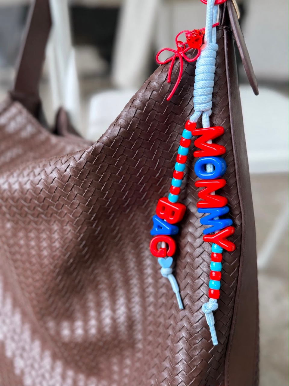 Colorful Mommy Bag charm with red letters attached to a woven brown bag